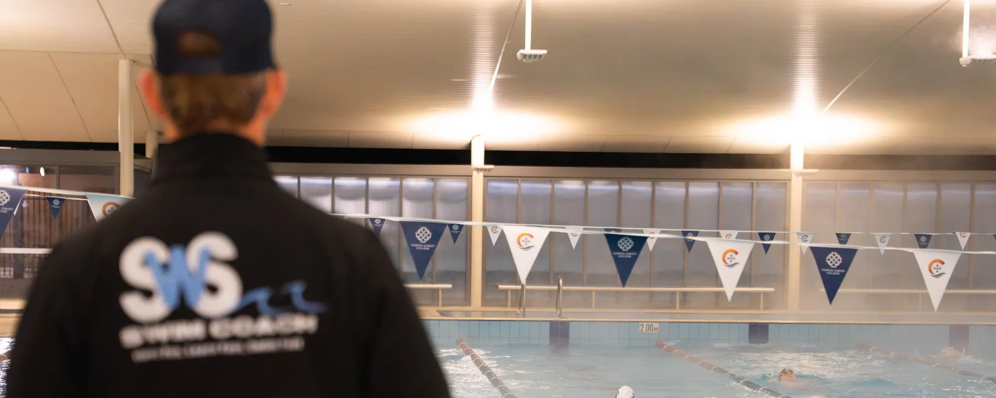 A Speed With Style coach in a branded jacket watching a squad session from the pool deck