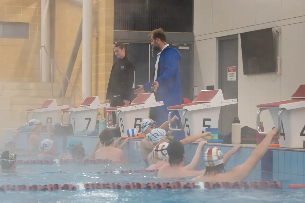Pre-squad swimmers at the wall being briefed by two coaches on the pool deck