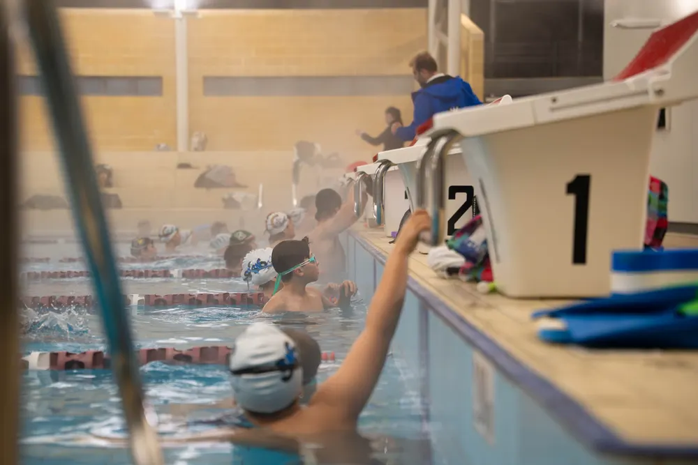 Squad swimmers in caps waiting at the starting blocks during a morning session